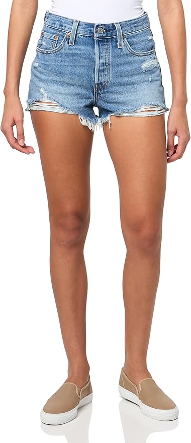 A person wearing distressed denim shorts paired with beige slip-on shoes.