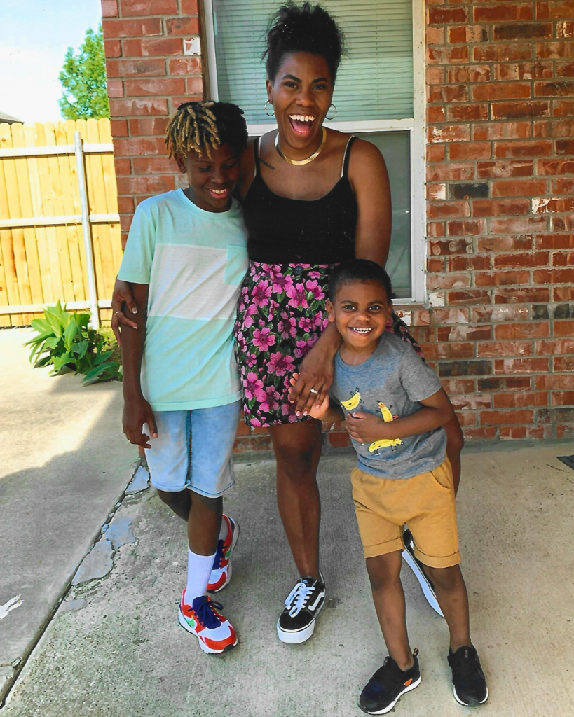 A joyful woman standing with two children outside a brick house, all smiling and posing for the camera.