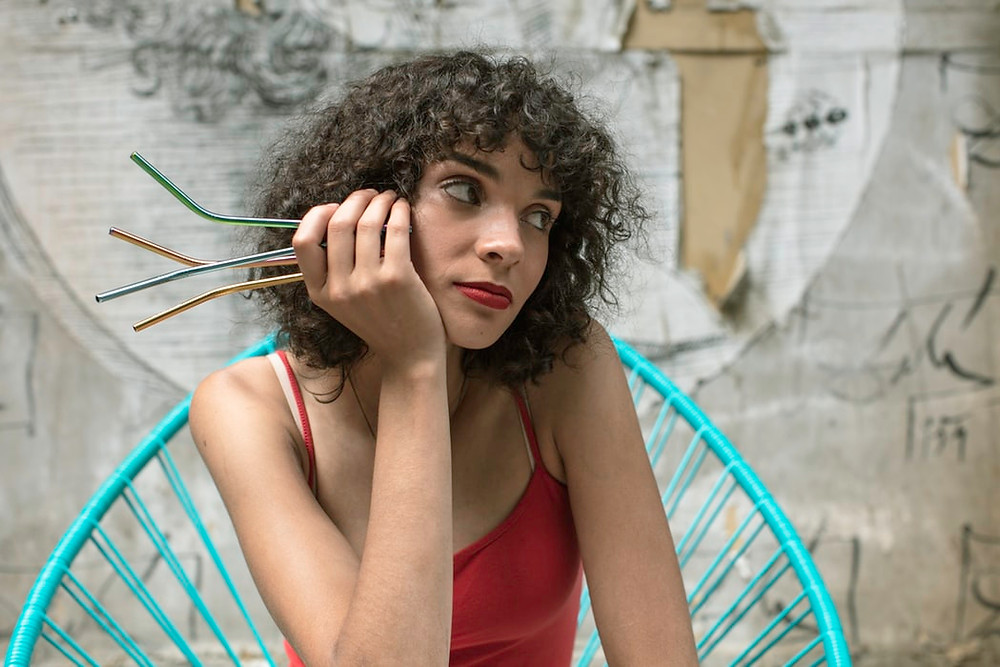 Woman wearing red tank top holding 4 reusable metal straws