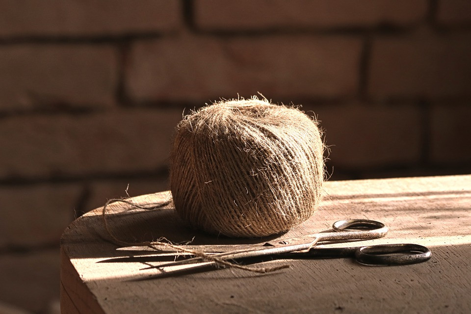 jute yarn spindle resting on a wooden table next to a pair of scissors