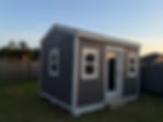 Small gray storage shed with white trim and a glass door.