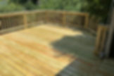 Newly constructed wooden deck with railings and leafy shadows.