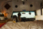 Cozy skoolie interior with panoramic waterfront view – A beautifully converted skoolie featuring a warm and inviting interior with a rustic wooden countertop, stylish kitchen sink, and soft lighting. A woman enjoys the stunning lakefront view from the driver’s seat, highlighting the freedom of vanlife and off-grid living.