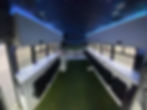 Fully converted skoolie with a stadium-style entertainment setup. The interior features a panoramic football field mural, green turf flooring, and blue LED accent lighting, creating the ultimate tailgating bus experience