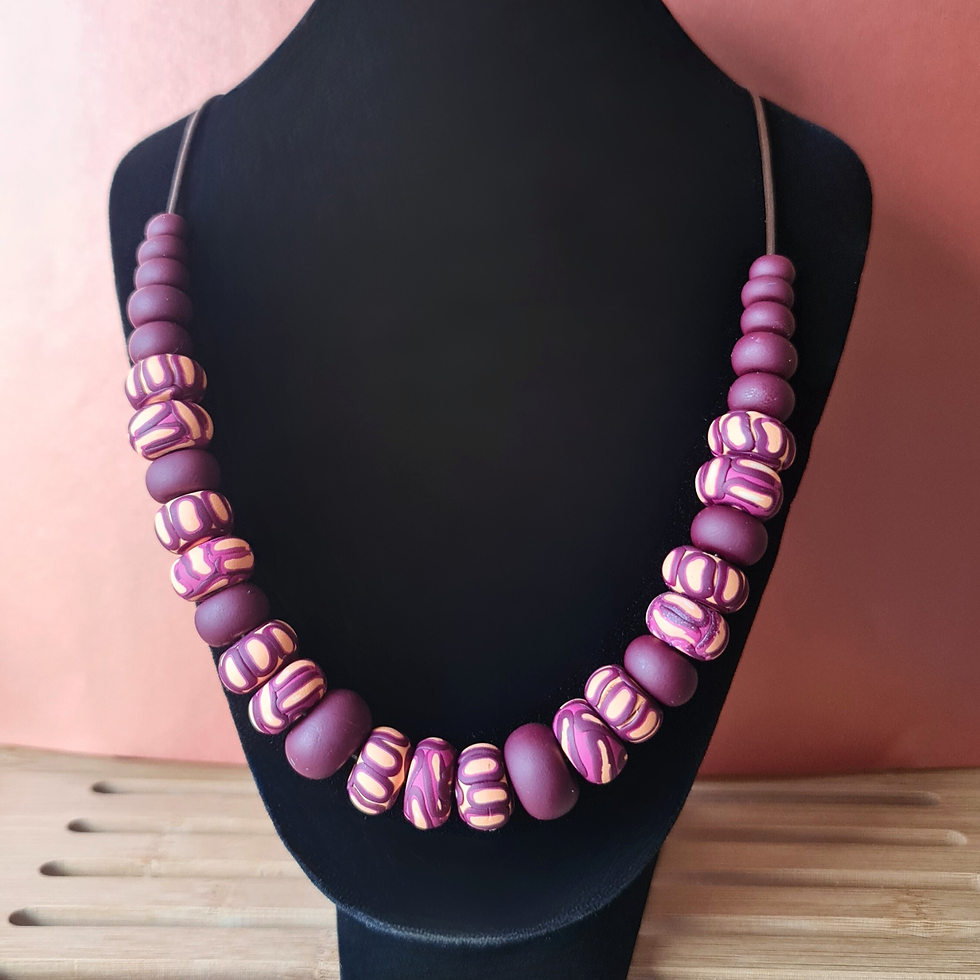Handmade polymer clay necklace in burgundy and plum tones displayed on a black jewellery bust against a warm terracotta backg