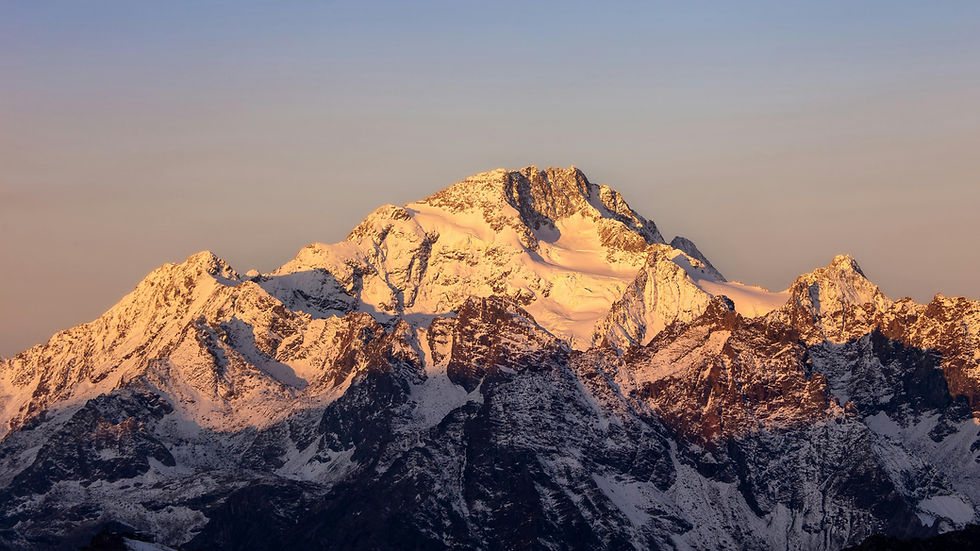 Snowy mountain peaks bathed in orange sunset light under a clear blue sky, creating a serene and majestic atmosphere.