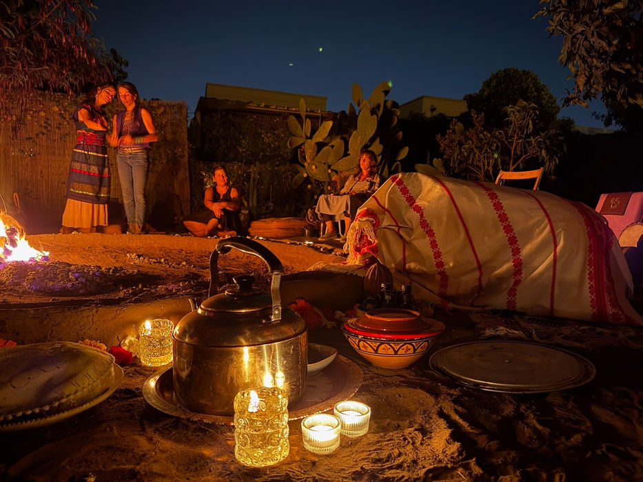 Women around a campfire brewing tea, warm lighting, night outside