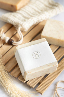 beige-handmade-soap-bar-with-blank-label-wooden-tray-near-soap-saver-bag-close-up