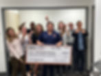 One man holding a big check with men and women behind