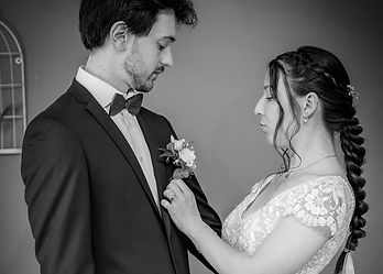 L'art des petits détails et des gestes simples. Pas de poses figées, juste de l'action, du vrai : la mariée qui réajuste délicatement la boutonnière de son mari lors de leur séance photo complice.