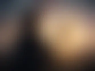 Une personne de dos tient un masque qui se désintègre en particules colorées, le soleil se couchant derrière offrant une lumière dorée.