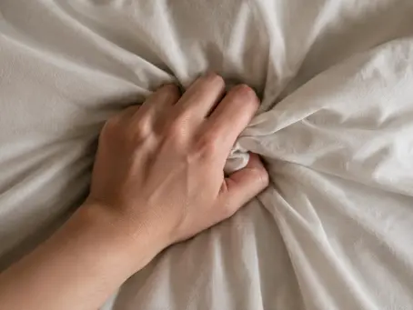 Une main saisit des draps blancs froissés, créant des plis et des textures.