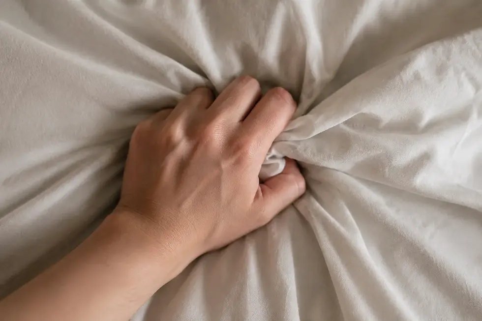 Une main saisit des draps blancs froissés, créant des plis et des textures.