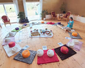 Frau sitzt in einem Kreis von Kissen, Meditation, Blumen auf dem Tisch.