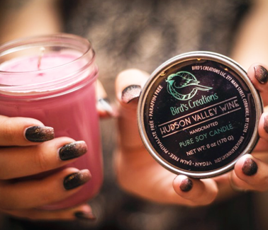Woman holding Bird's Creations Hudson Valley Wine candle with visible text on label