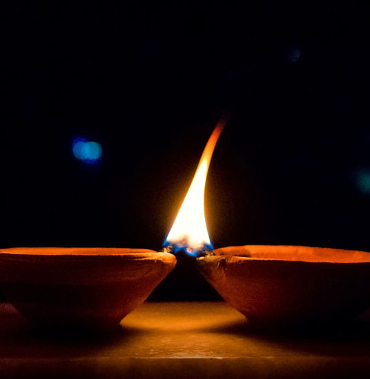 Two clay diya lamps with a single glowing flame representing relationship astrology and self-awareness.