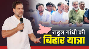 Man in white shirt speaking with microphone; background of people standing, text reads "राहुल गांधी की बिहार यात्रा" in Hindi.