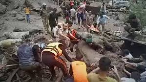 People in rescue gear and uniforms work together in a muddy, debris-filled area, conveying urgency and teamwork amid disaster aftermath.