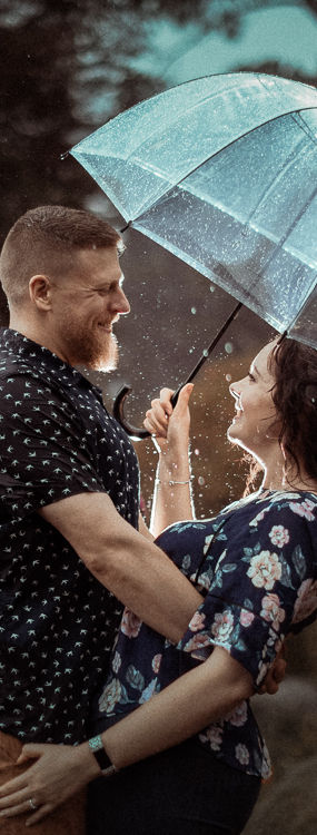 Rainy romance: Chris and Loran's engagement photo in the rain at Wellington Botanical Garden. Loran holds an umbrella, and Chris supports her, creating a shining moment of love. Photographed by Kent Chua Photographer, Wellington Wedding Photographer.