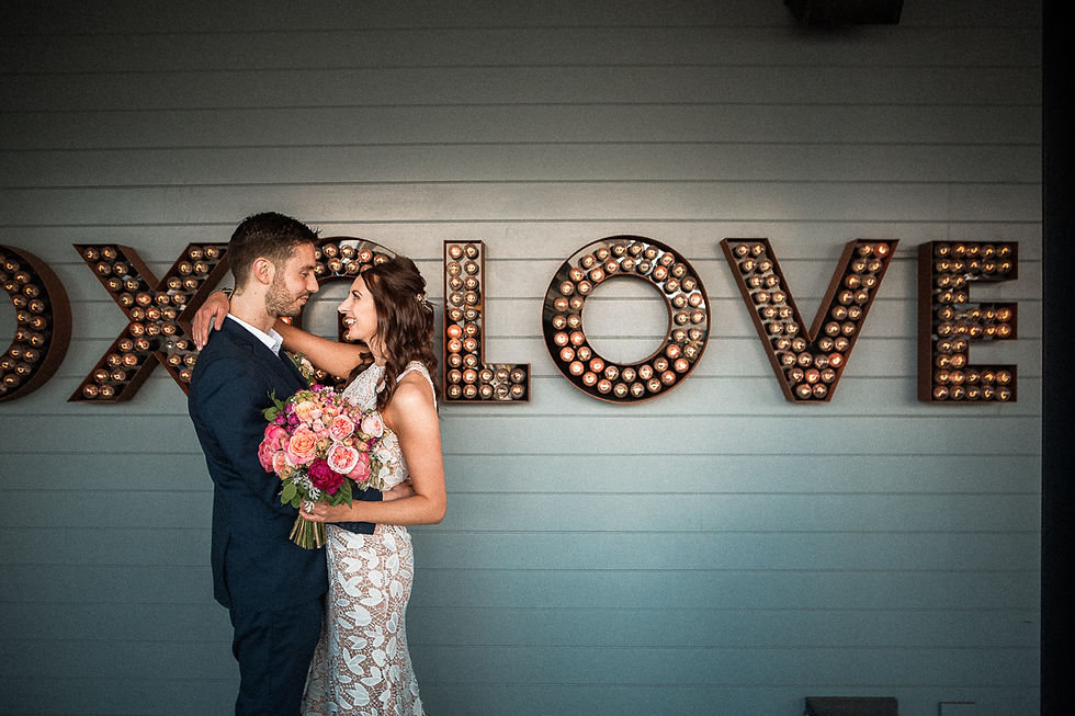 Radiant love captured as the wedding couple poses in front of the Foxgloves Bar & Kitchen sign on the Wellington waterfront. The sleek design and waterfront backdrop frame the joyous moment of their special day.