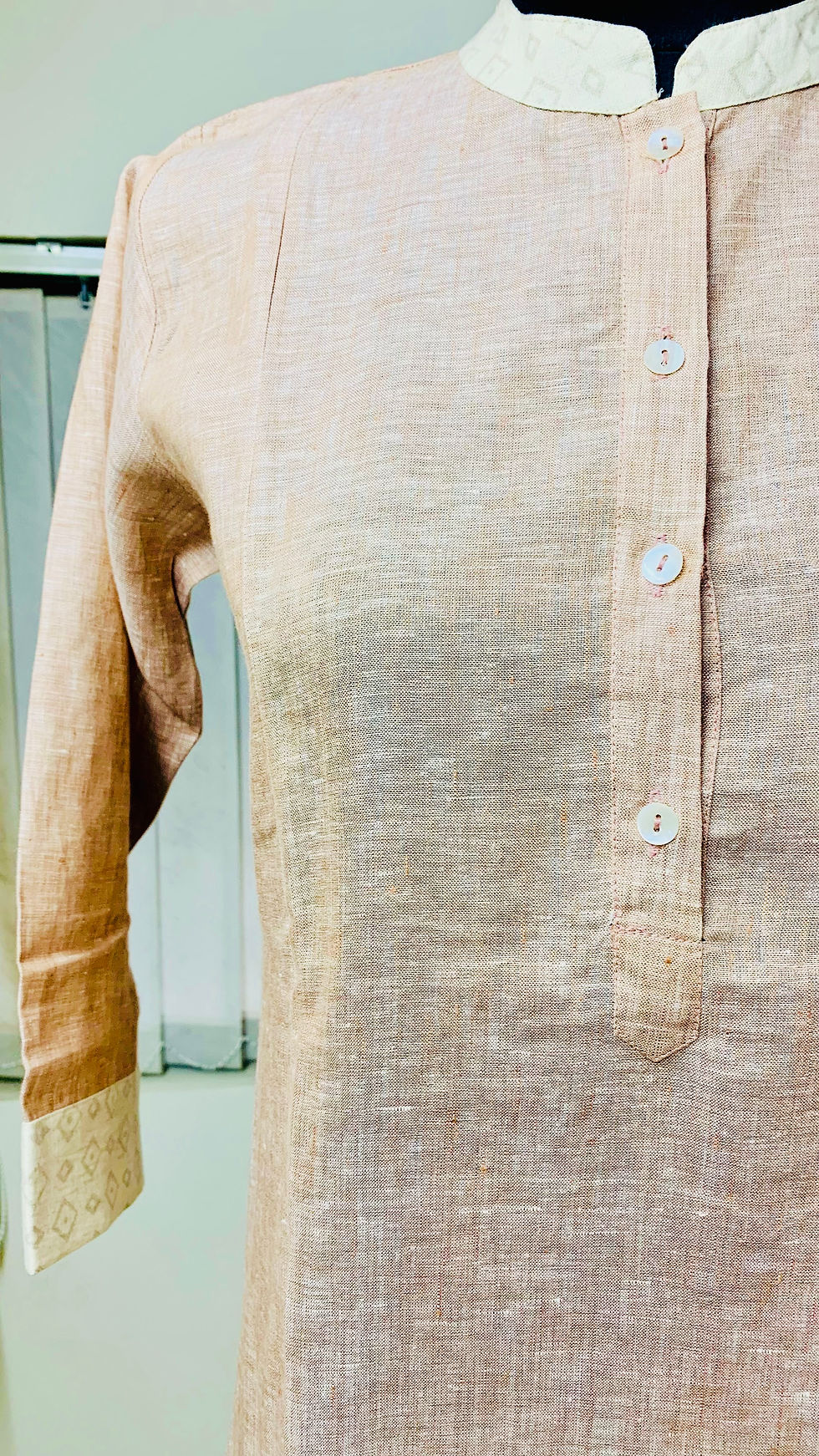 Close-up of a women's light peach pure linen kurta tunic on a mannequin, featuring a contrast printed mandarin collar and sleeve cuffs, white buttons, and a soft, breathable texture with subtle woven details