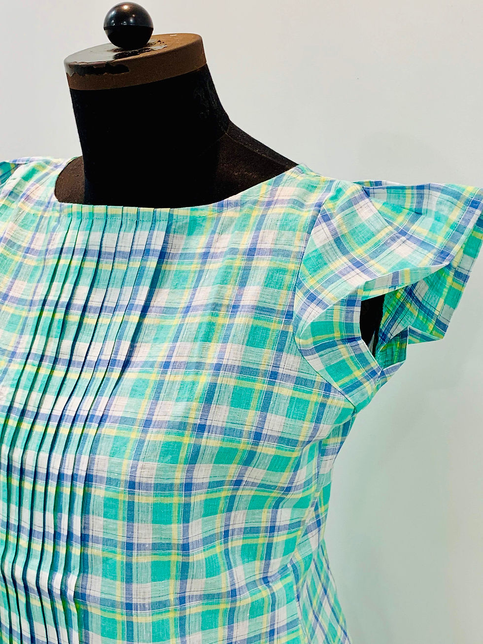 Model wearing a sea green checkered linen top from Azitiz, featuring cap sleeves and pleated front