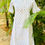 Thumbnail: A mannequin in a white printed dress with ruffled sleeves and button details, set against lush green foliage.