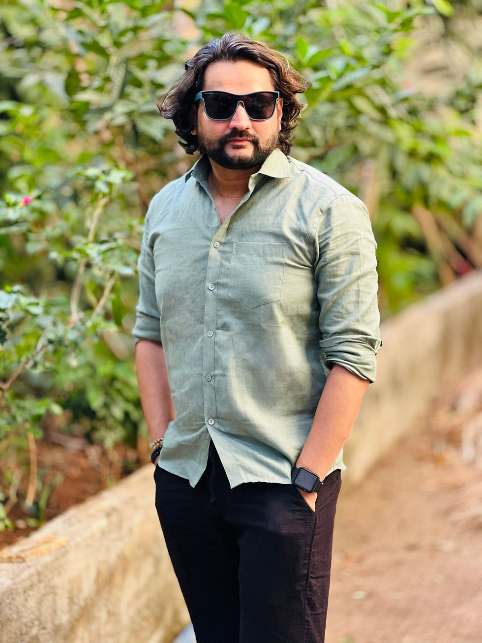 Thumbnail: Man in sunglasses, sage green linen shirt, and black pants standing outdoors by greenery.