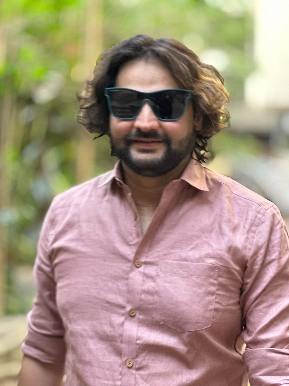 Thumbnail: Man smiling in a dusty rose pink linen shirt and sunglasses, standing outdoors with a blurred green background.