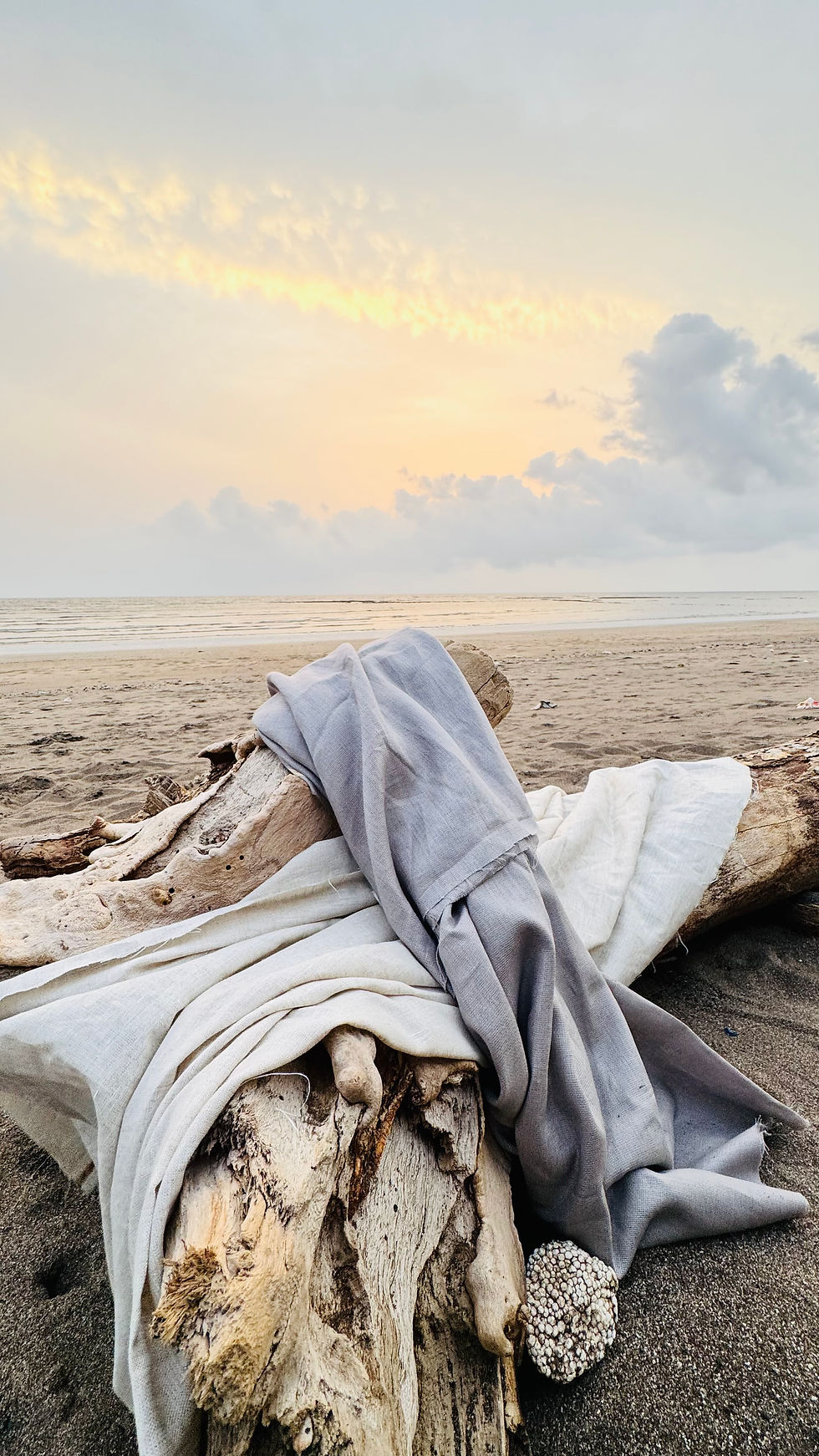 Light grey and beige coloured linen fabric lying wrapped on an old tree trunk lying on a beach