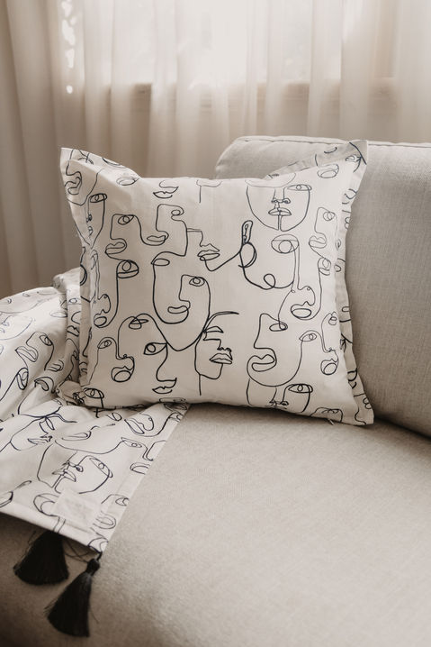 Soulty Tribe Threads Home Decor - Faces Square Cushion with Flange and Throw with Tassels Combo on couch in front of window with sheer curtains.