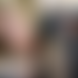 Una mujer rubia pensativa en interior y un hombre barbudo con sombrero gris en un entorno medieval. Emoción de reflexión y misticismo.