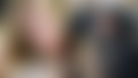 Una mujer rubia pensativa en interior y un hombre barbudo con sombrero gris en un entorno medieval. Emoción de reflexión y misticismo.