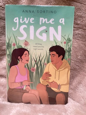 Cover of Give Me a Sign by Anna Sortino: female and male sitting outdoors using ASL signs, "All they need are the right words."