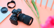 The Tamron 25-200mm F/2.8-5.6 Di III VXD G2 mounted on a Sony full-frame body, lying on a pink surface beside its lens cap and hood.