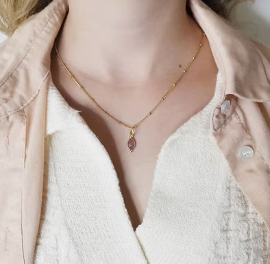 Gros plan d’un cou avec collier doré et pendentif violet, sur top crème et chemise beige.