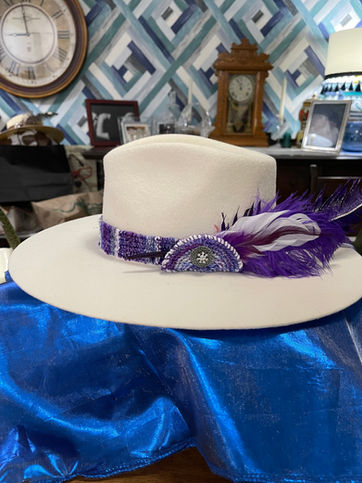 white hat with woven band purple hay band and white and purple feathers.
