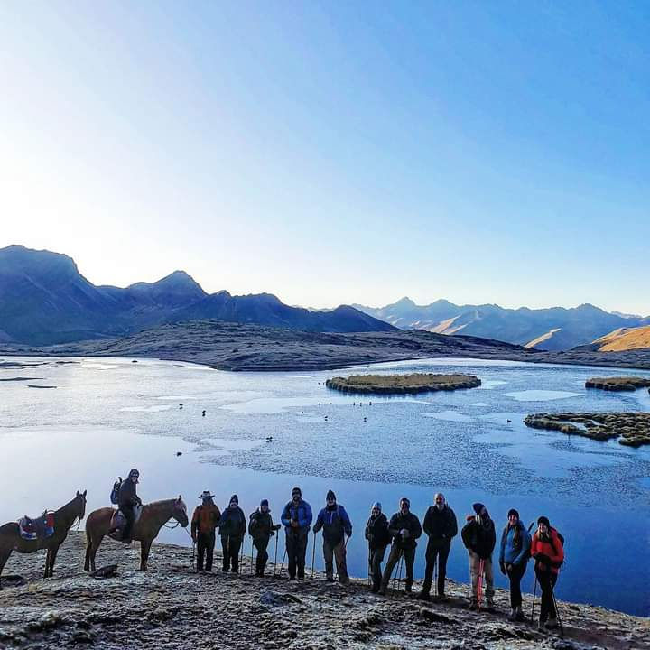 Thumbnail: Several hikers and two horses standing by a mountain lake in Peru during a sunrise.