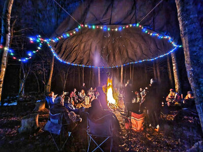 Group of people winter camping and sitting by a fire underneath a large parachute shelter