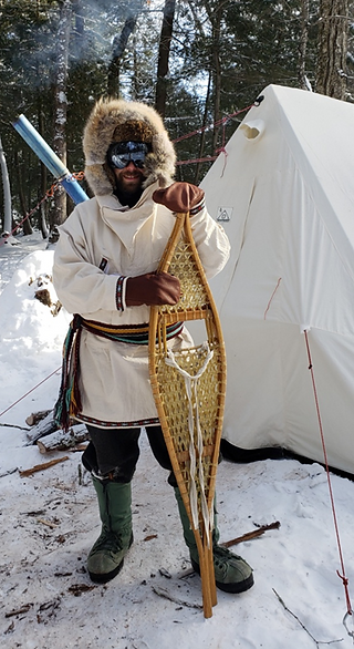 Nick Gordon wearing traditional wool pants and a canvas anorak holding traditional Ojibwa snowshoes while winter camping.