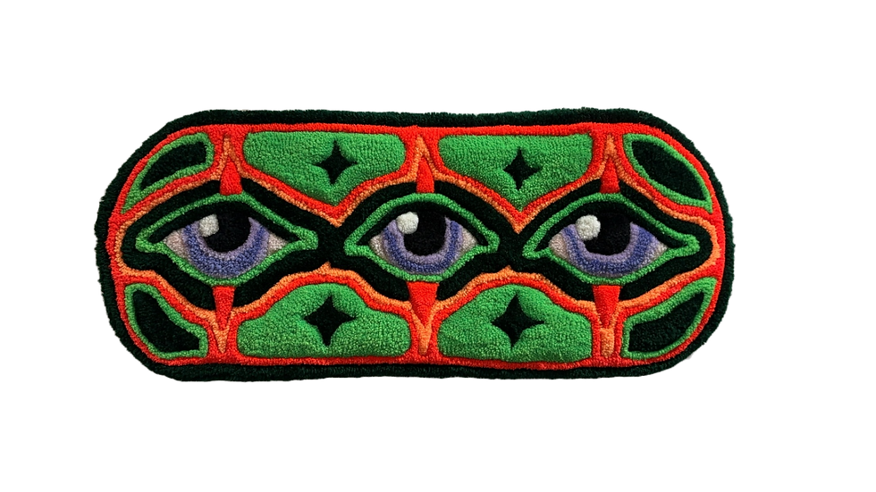Tufted artwork of three blue-colored eyes in a row. The artwork is a long oval shape and there are orange and green borders surrounding the eyes.