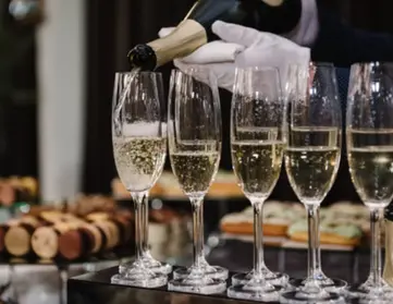 Focused shot of bartender wearing white gloves pouring champagne flutes. 
