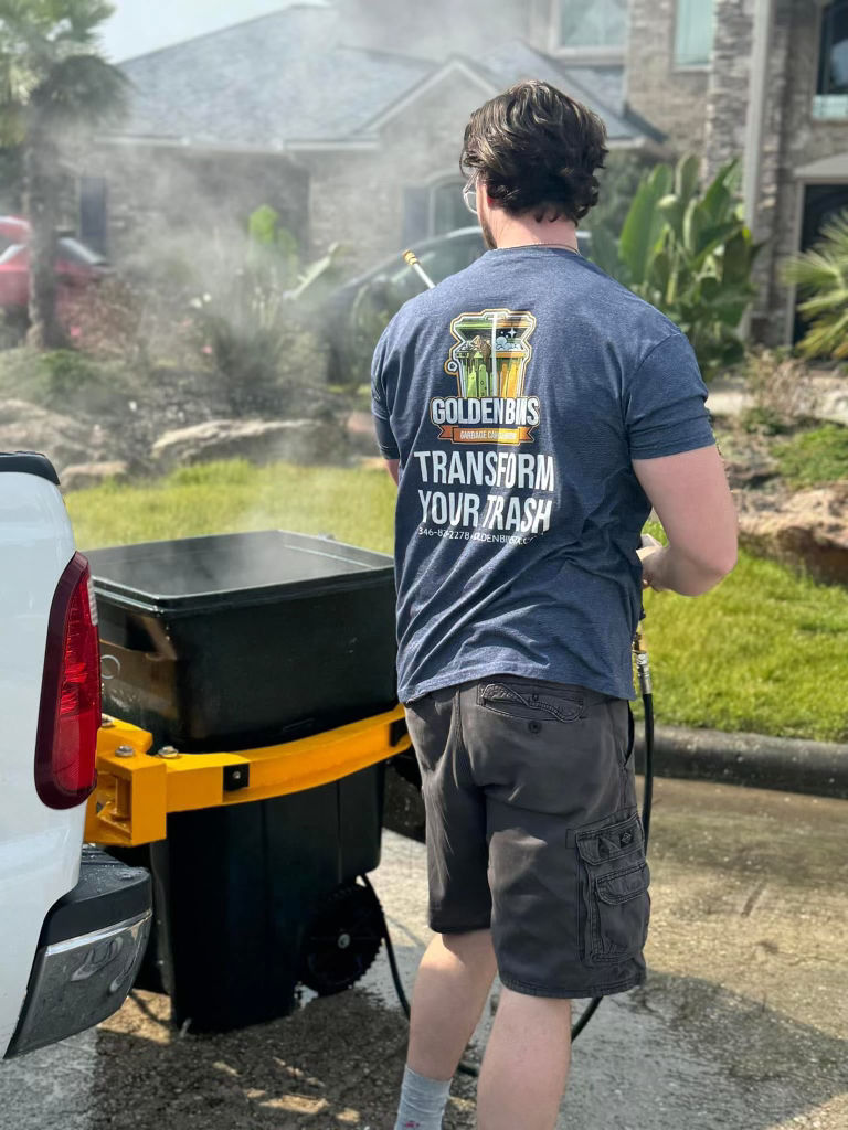 High angle view of a professional cleaning a large commercial garbage bin with a pressure washer