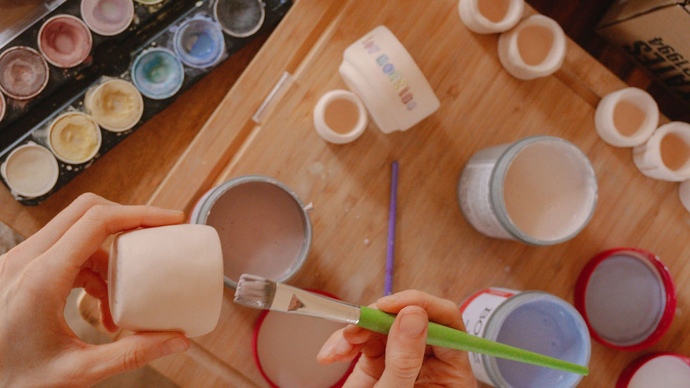 Hands painting ceramic pots with a variety of pastel colors, showcasing a creative art workshop.