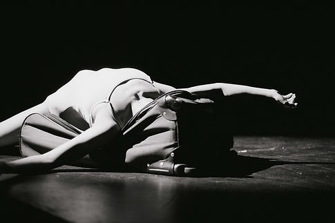 black and white photo of dancer laying in a suitcase, her head and face hidden