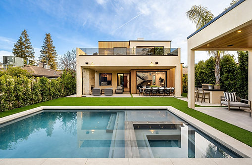 Modern luxury house with a swimming pool, outdoor seating, and lush greenery under a clear