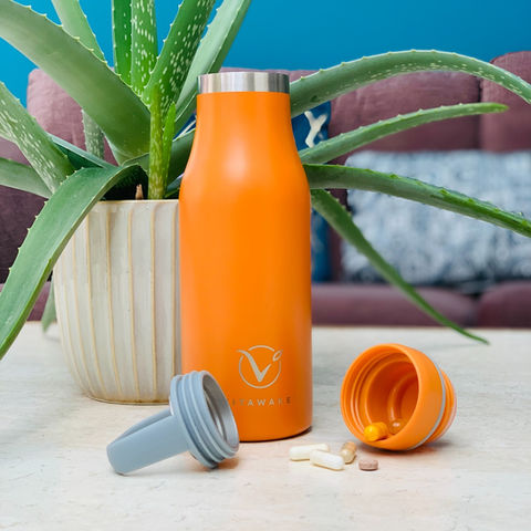 VitaBottle on table with lid and pill compartment open and supplements falling out of lid