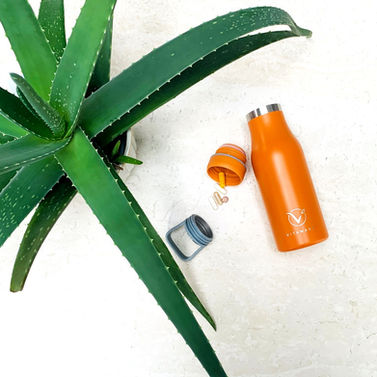 Top eye view of opened VitaBottle with pills falling out of lid next to aloe vera plant