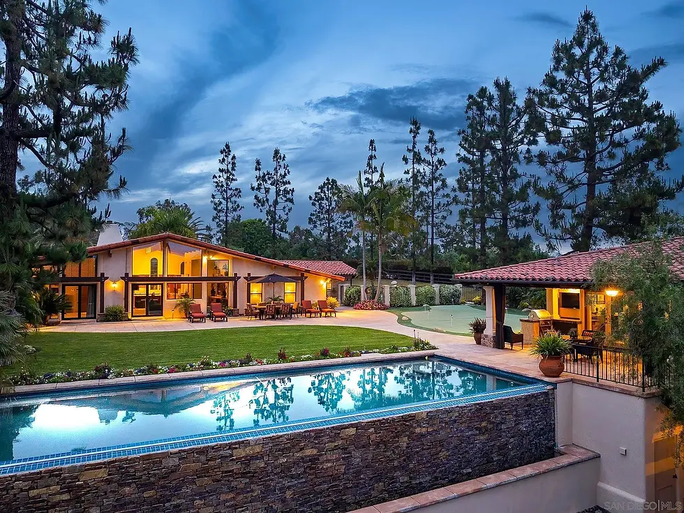 A luxurious house with warm lights, a patio, and a pool in a landscaped yard. Surrounded by tall trees under a twilight sky. Relaxed ambiance.