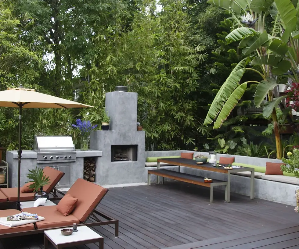 Outdoor patio with brown loungers, umbrella, grill, and fireplace. Surrounded by lush green plants and trees, creating a serene atmosphere.
